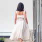 beautiful woman in a white two piece dress with corset top with a ruffle over the breast seam and long flowy skirt. this picture is made from the back, walking away