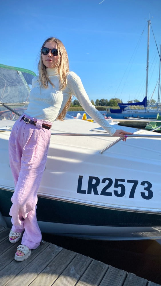 lady with pink pants and white turtleneck by the boat in sunglasses