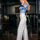 beautiful blond lady in a colorful baby blue top and white checked pants. dress with feathers on the sleeves