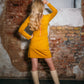 Beautiful blond woman in a mustard yellow two-piece dress with ruffle. She is wearing white boots