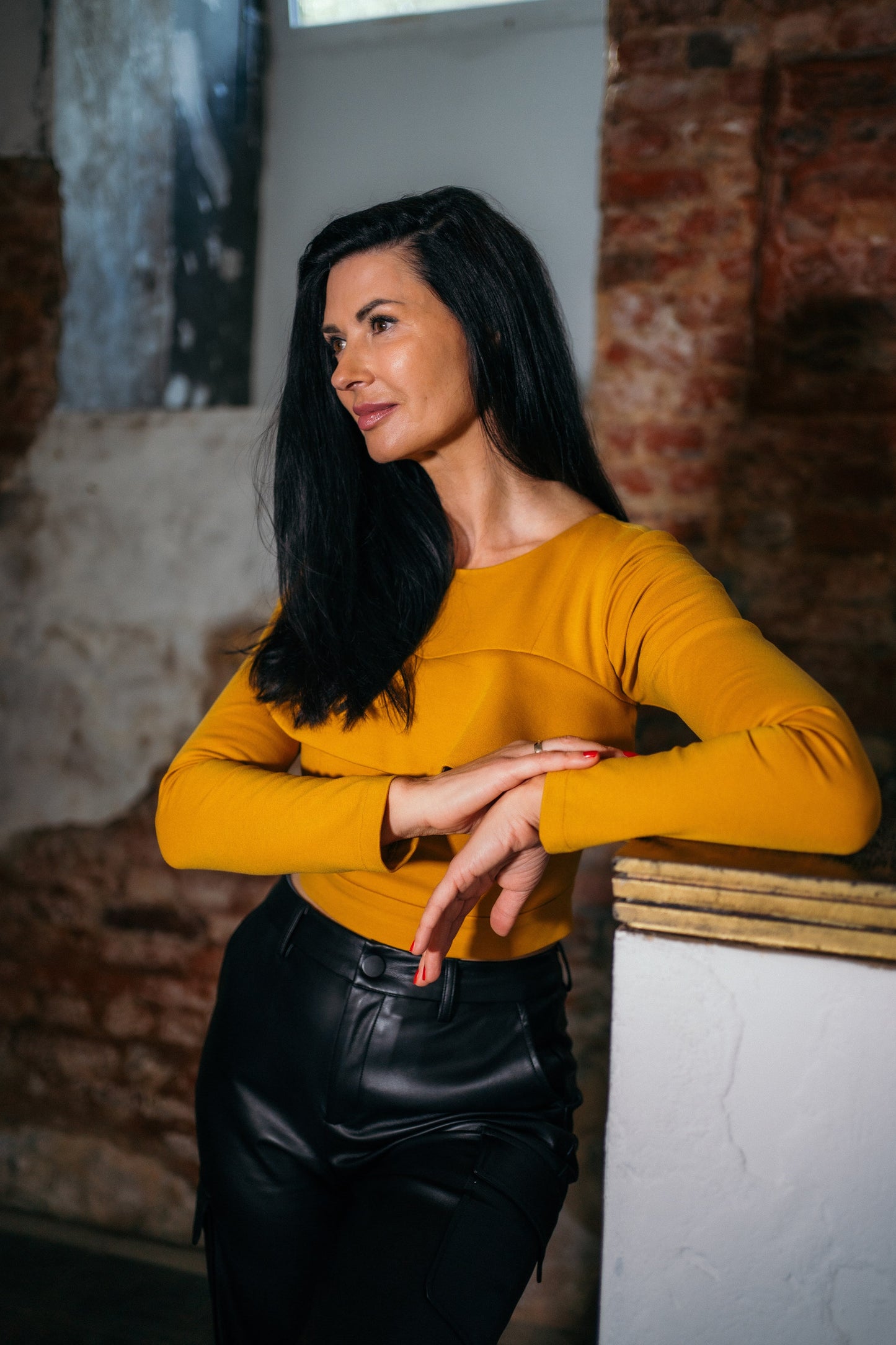 Beautiful black haired woman wearing mustard yellow top with ruffle and black leather pants