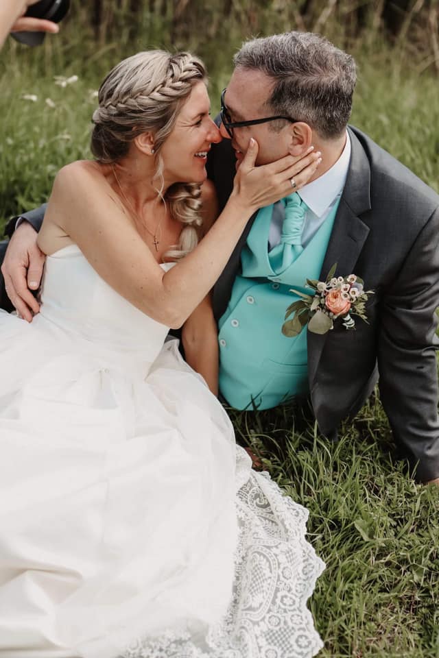 couple kissing on their wedding day, sitting in the grass