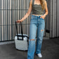 beautiful blonde woman with a suitcase in her travel friendly corset top in a gray color together with a pair of jeans and white sneakers