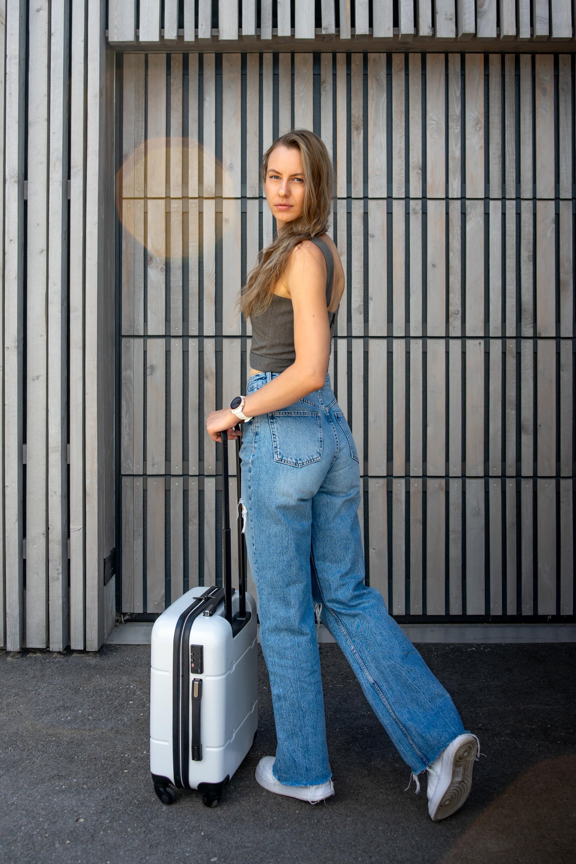a beautiful lady running to her plane with her suitcase in a gray corset top, jeans, white sneakers