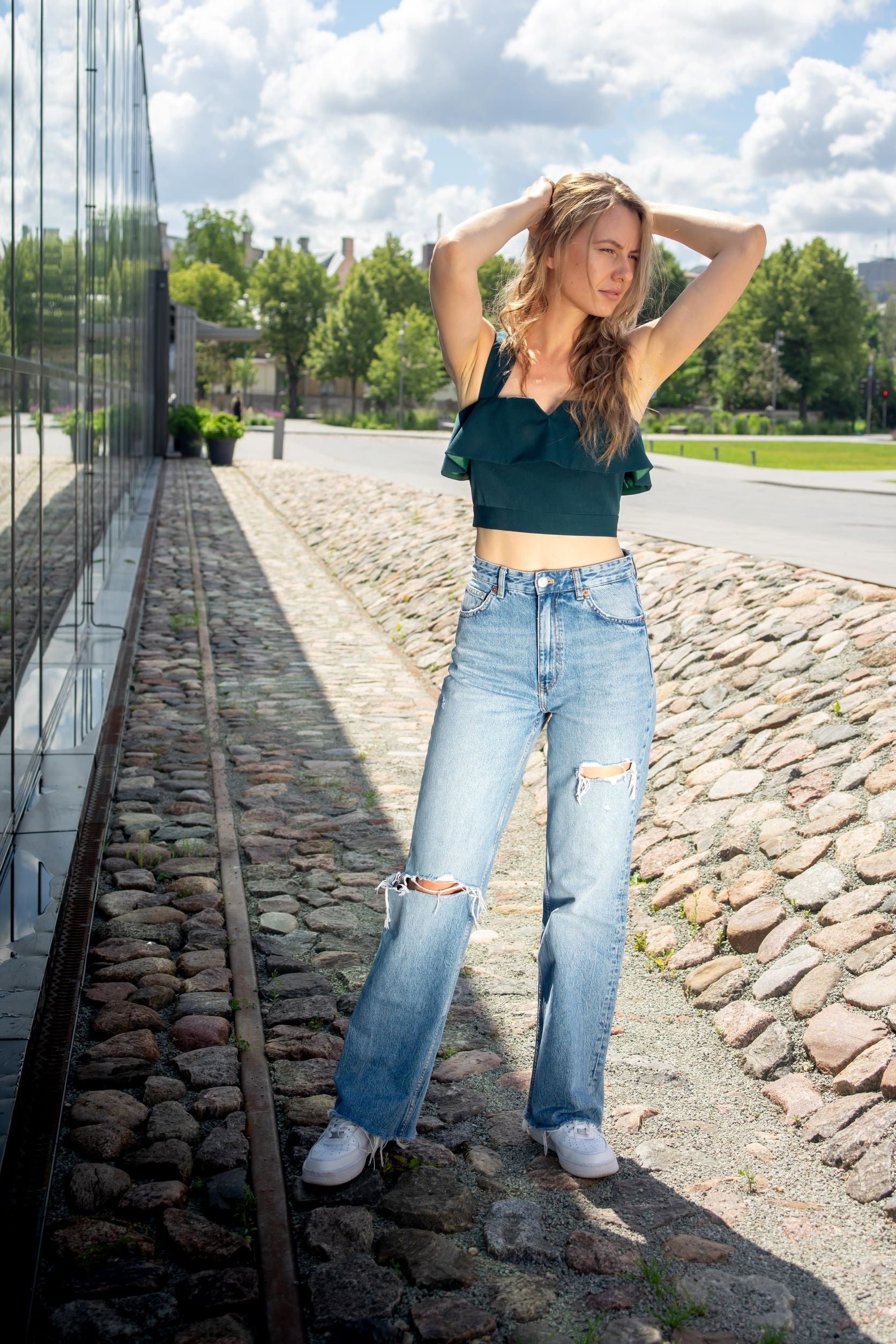 lady in an emerald green ruffled top and jeans and white sneakers