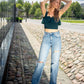lady outdoors on a sunny day wearing emerald green ruffled top with jeans and white sneakers