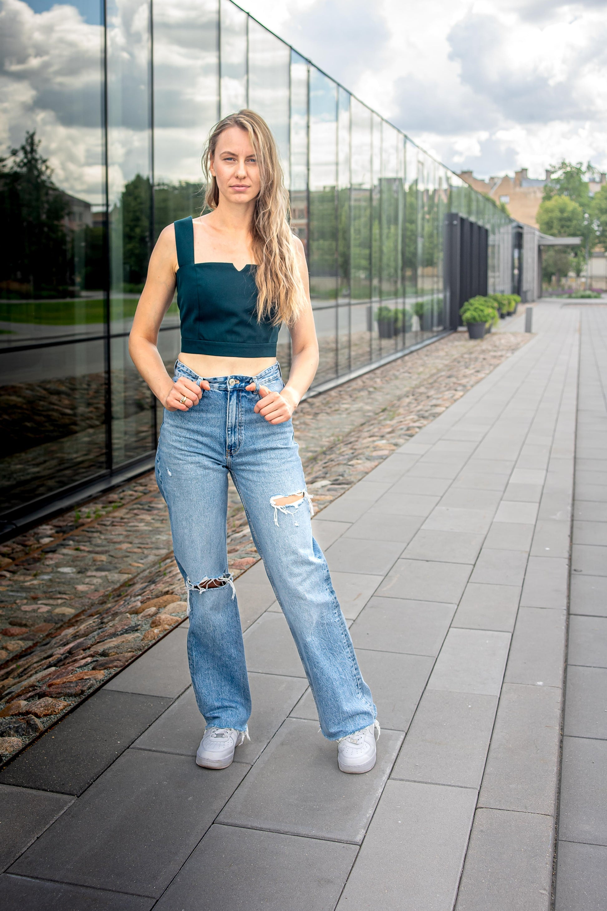 blonde woman on a sunny day in en emerald green corset top, paired with jeans and white sneakers
