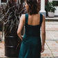 beautiful brunette on the streets walk in an emerald green two-piece mini dress, that consists of a corset top and a mini skirt, paired with black heels. this picture is made from the back