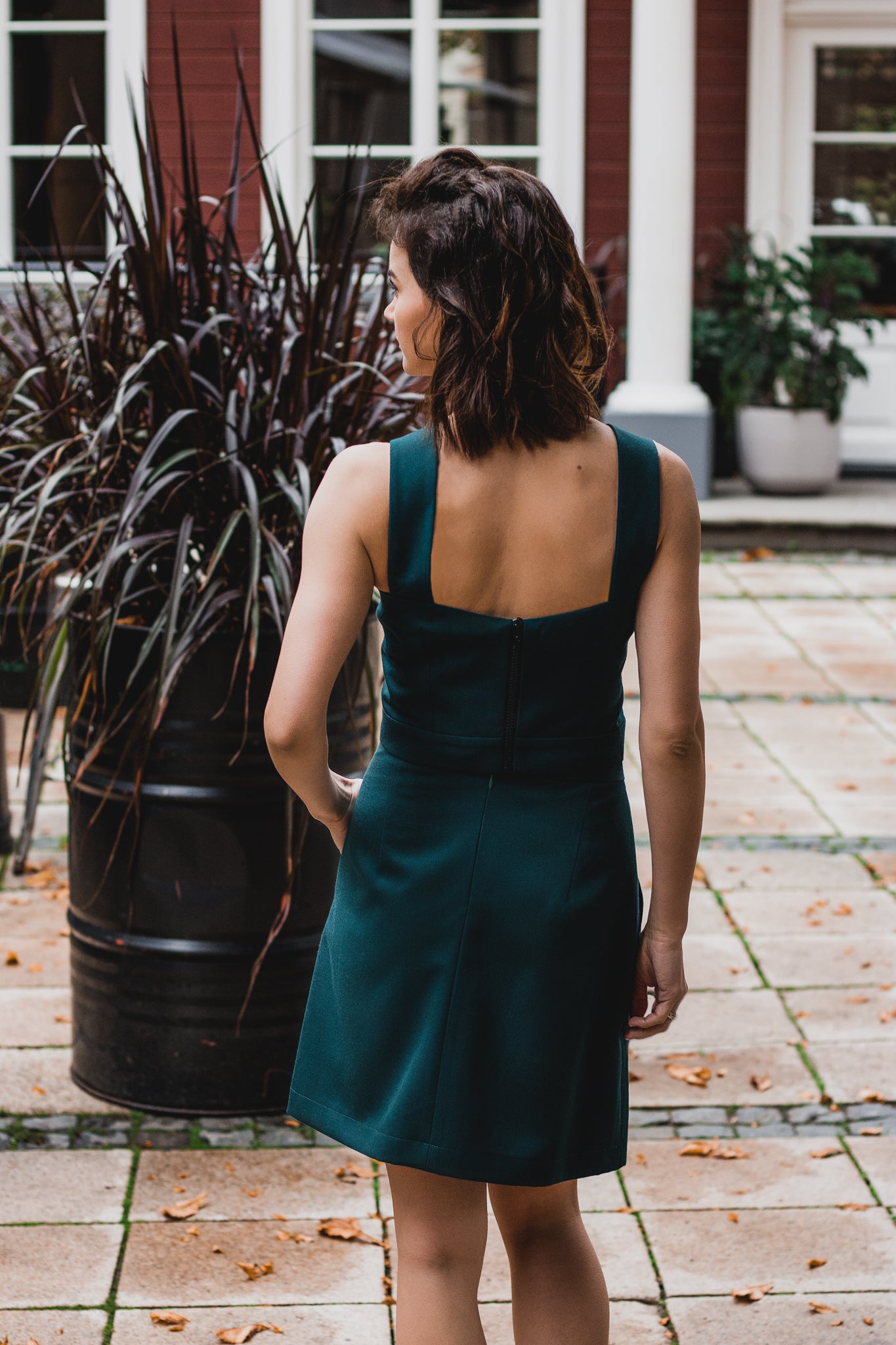 beautiful brunette on the streets walk in an emerald green two-piece mini dress, that consists of a corset top and a mini skirt, paired with black heels. this picture is made from the back
