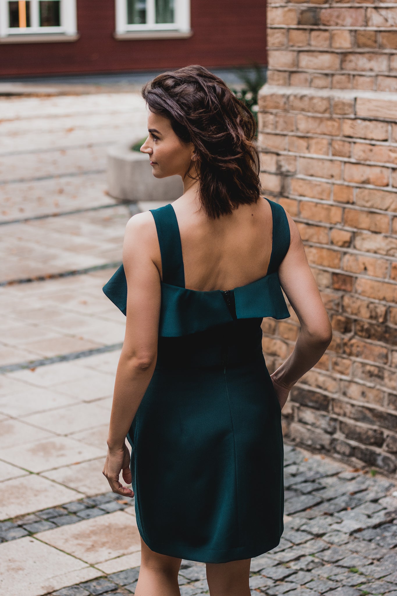 beautiful lady from the back in an emerald green two-piece dress, that consists of a ruffled top and a mini skirt with pockets