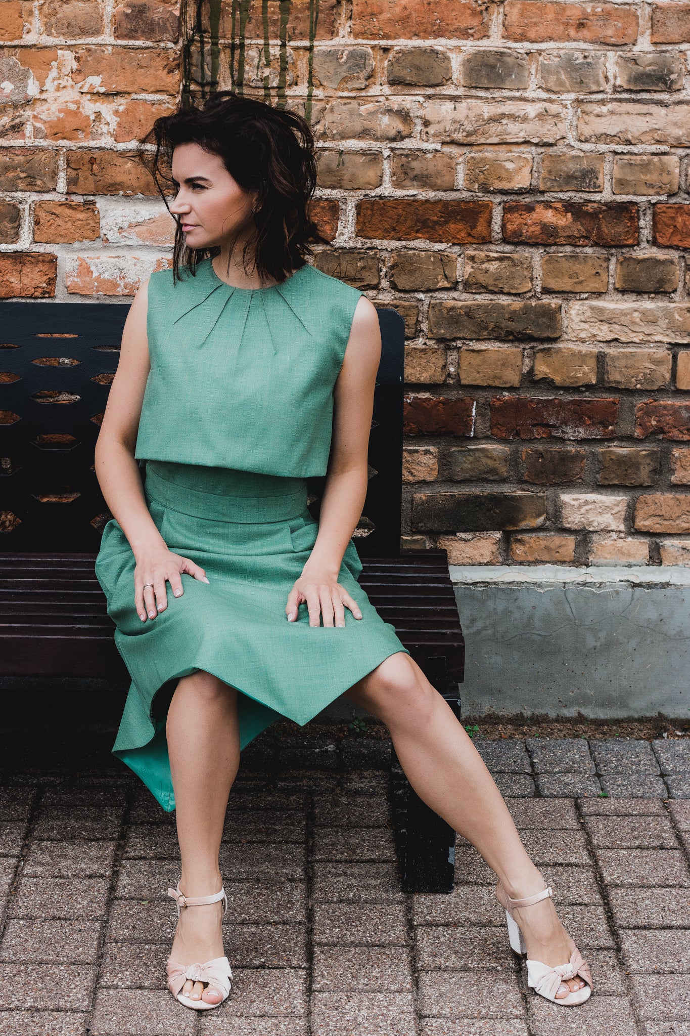 beautiful woman sitting on a bench in mint green three-piece dress set smiling over the shoulder. triangle skirt