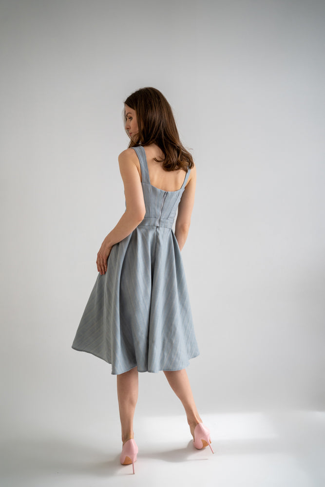 beautiful lady in a white studio wearing light blue two-piece dress, that consists of a corset top with or without nursing option and a flowy skirt, pink heels. this picture is taken from the back and the lady has a dreamy look