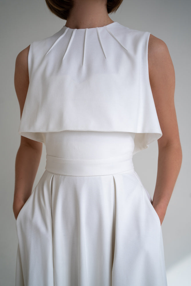 Clear white overtop can be worn over tops and blouses, great for discreet nursing. This piece of clothing is a separate part of the transformable dress set so later on you can add any top and skirt of your choice and build your own capsule pieces. The overtop will be a perfect eye-catching element that will make your wardrobe unique. Lady in a white vest, overtop, with hands in pockets.